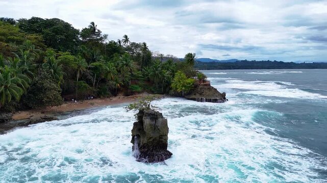 Aerial view of Refugio Nacional Gandoca-Manzanillo with crashing waves against a rocky outcrop and lush tropical palm forest along the coastline in Limon, Costa Rica.