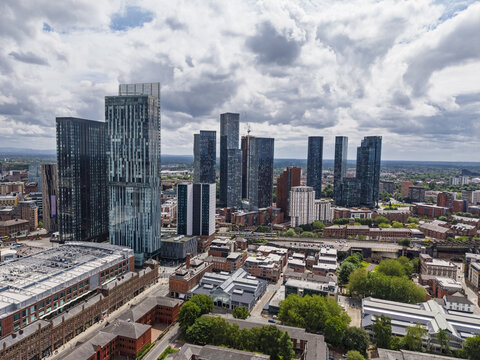 Aerial view of the modern skyline of Manchester featuring glass skyscrapers and urban architecture under a cloudy sky in Manchester, England, United Kingdom.