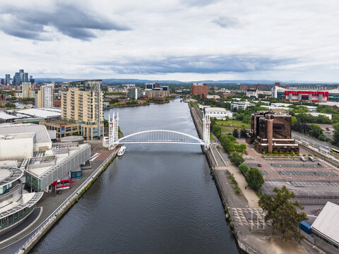 Aerial view of the Millennium Bridge spanning the Manchester Ship Canal, surrounded by modern office buildings and urban infrastructure in Manchester, England, United Kingdom.