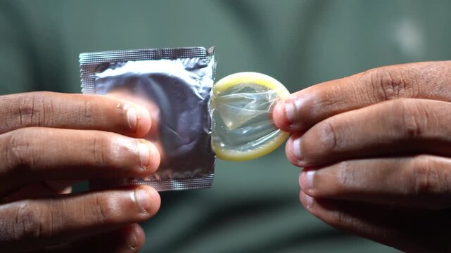 Man taking latex condom out of open silver wrapper close up view for birth control awareness. opening silver condom wrapper for safe sex and STD prevention concept.