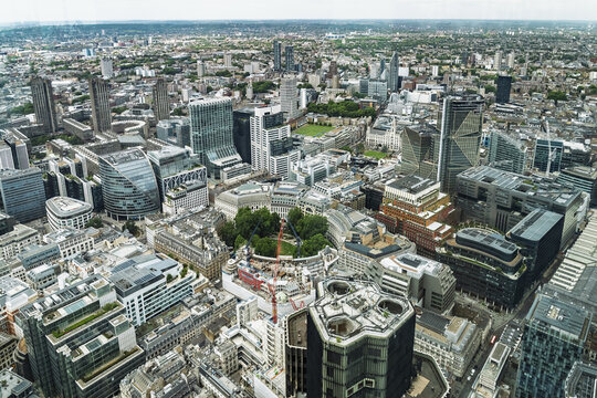 Aerial view of the dense urban landscape of London featuring modern skyscrapers, historic architecture, and a central green space with construction cranes in London, England, United Kingdom.