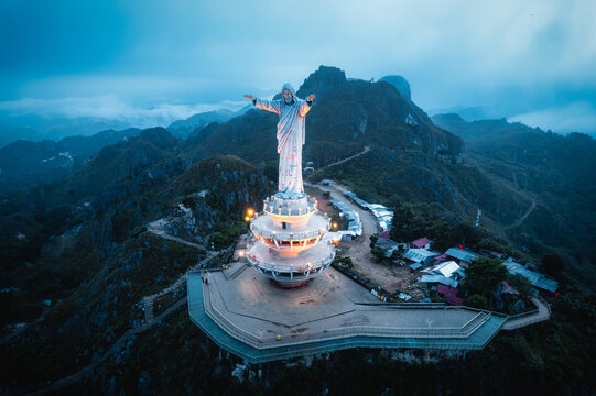 Aerial view of the Jesus Christ Blessing Statue standing atop Buntu Burake hill, surrounded by misty mountains and lush green landscape in Makale, South Sulawesi, Indonesia.