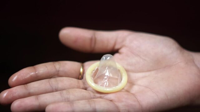 unrolled latex condom resting on open female palm over dark background. transparent condom in open hand illustrating sexual health awareness. 