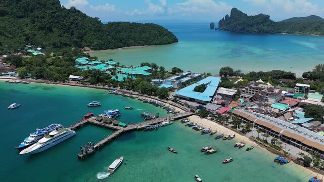 Aerial view of Phi Phi Islands featuring a busy pier with boats, turquoise water, sandy beach, and coastal buildings in Mueang Krabi District, Krabi, Thailand.