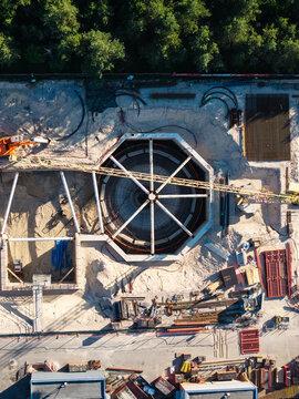 Aerial view of the Daugavgriva Wastewater Treatment Plant construction site featuring an octagonal concrete basin, a crane, and scattered building materials in Riga, Latvia.