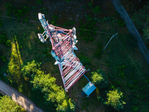 Aerial view of a telecommunications tower with antennas surrounded by green trees and a dirt path in Riga, Latvia.