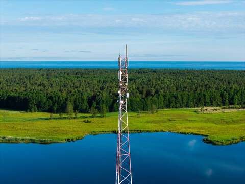Aerial view of a telecommunications tower standing near the Bullupe River, surrounded by lush green forests and blue water in Riga, Latvia.