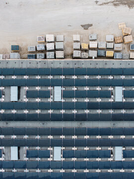 Aerial view of a manufacturing facility with rows of stacked concrete paving stones and construction materials alongside a large roof covered in solar panels in Riga, Latvia.