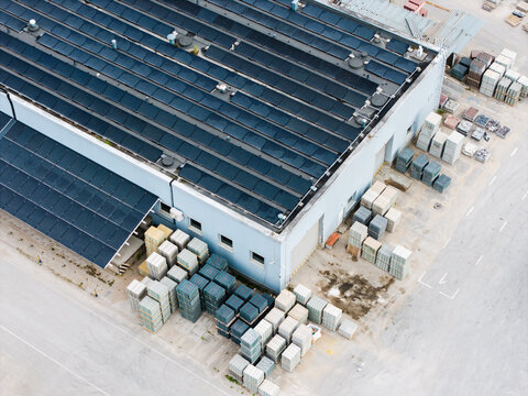 Aerial view of a manufacturing facility featuring a large roof covered in solar panels and stacks of concrete paving stones stored in the yard in Riga, Latvia.