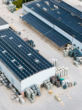 Aerial view of a concrete manufacturing facility with solar panels on the roofs and stacks of paving stones and construction materials in the yard in Riga, Latvia.