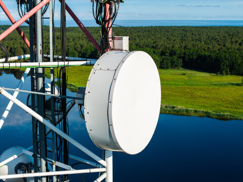Aerial view of a large white parabolic antenna mounted on a telecommunications tower overlooking the Bullupe River with lush green banks and forest in Riga, Latvia.
