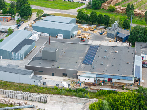 Aerial view of a manufacturing plant producing wood-based materials like chipboard and MDF, featuring industrial warehouses, storage areas with stacked panels, and solar panels in Riga, Latvia.