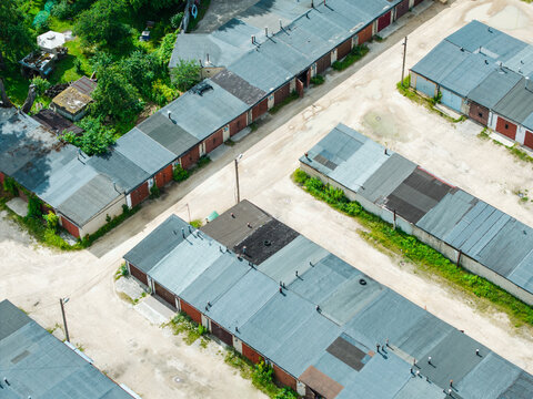Aerial view of a complex of garage units with flat roofs, separated by dirt paths and patches of green vegetation in Riga, Latvia.