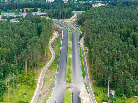 Aerial view of the newly built Janis Cakste Avenue, a major arterial road cutting through a dense pine forest, connecting the Southern Bridge transport corridor in Riga, Latvia.