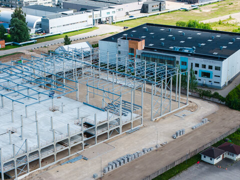 Riga, Latvia - 05 July 2026: Aerial view of a construction site featuring a steel frame structure for a new industrial building, surrounded by paved areas and existing commercial facilities.