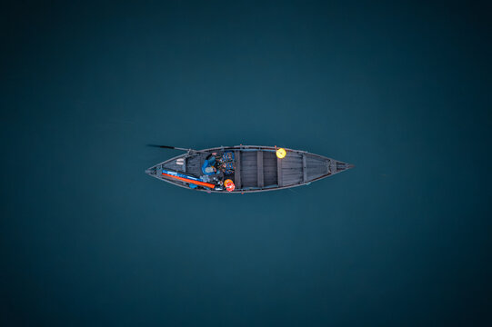Aerial view of a small wooden boat floating on the calm dark water of the Thu Bon River with a person sitting inside near the Lantern Riverside in Hoi An, Da Nang, Vietnam.