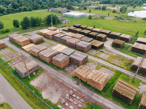 Aerial view of stacks of timber and lumber stored in an industrial yard, surrounded by green fields and trees in Brankas, Jelgava Municipality, Latvia.