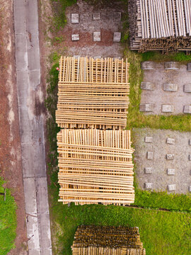 Aerial view of stacked timber logs in a forestry yard with concrete foundations and a nearby road in Brankas, Jelgava Municipality, Latvia.