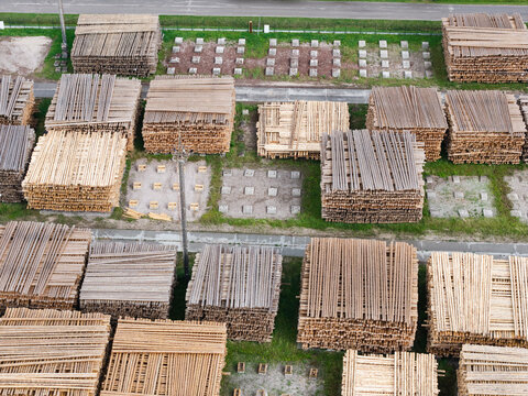 Aerial view of large stacks of sawn timber arranged in an industrial yard with concrete foundations and patches of grass in Jelgava Municipality, Latvia.