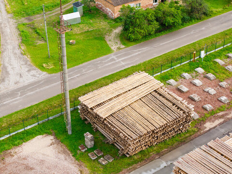 Aerial view of a large stack of timber logs stored in an industrial yard near a road and a tall utility pole in Latvia.