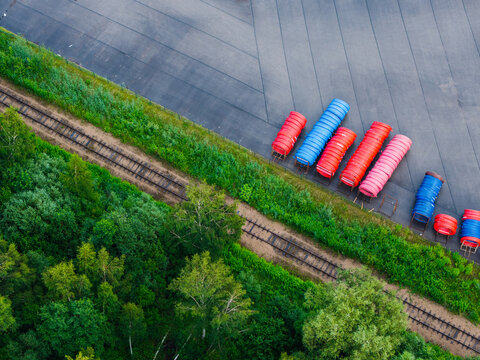Aerial view of stacks of colorful plastic pipes stored at a manufacturing facility near railway tracks and lush green forest in Jelgava, Latvia.