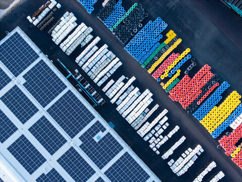 Aerial view of a polymer pipe manufacturing facility featuring rows of colorful plastic pipe coils and a large solar panel array on the roof in Jelgava, Latvia.