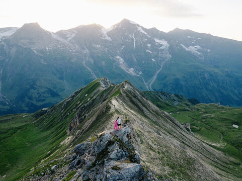 Aerial view of a couple standing on the rocky summit ridge of Edelweissspitze with green mountain slopes and distant peaks in Fusch an der Grossglocknerstrasse, Salzburg, Austria.