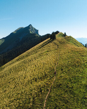 Aerial view of the Hardergrat mountain ridge trail with a hiker walking along the grassy path under a clear blue sky in Habkern, Bern, Switzerland.