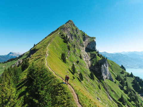 Aerial view of the Hardergrat mountain ridge trail with hikers walking along the path, surrounded by green alpine slopes and rocky peaks in Habkern, Bern, Switzerland.