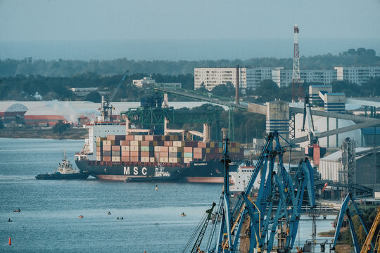 Riga, Latvia - 04 September 2020: Aerial view of a large MSC container ship docked at the port, surrounded by industrial cranes, loading equipment, and urban buildings in the background.