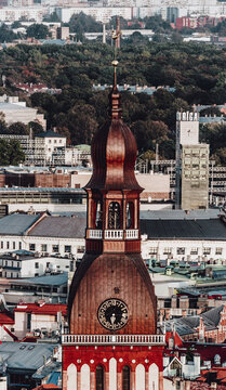 Aerial view of the historic Riga Cathedral spire with its clock face and copper roof rising above the surrounding urban rooftops in Riga, Latvia.