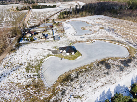 Aerial view of ponds shaped like the map of Latvia, a house with solar panels, and snow-covered fields in Latvia.