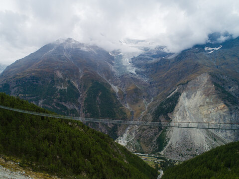 Aerial view of Charles Kuonen Suspension Bridge spanning the valley with alpine mountains and forest in the background in Randa, Valais, Switzerland.