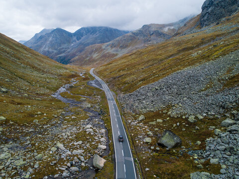 Aerial view of the winding road through the Fluela Pass with a car driving near the Susasca river, surrounded by rocky mountain slopes and alpine terrain in Davos, Graubunden, Switzerland.