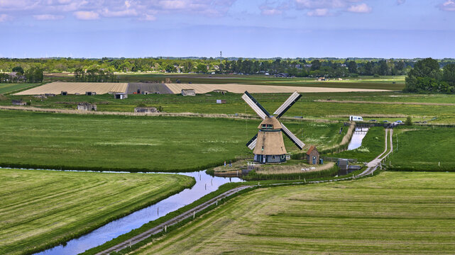 Bergen, Netherlands - 09 May 2026: Aerial view of the Windmill of the Philisteinsche Polder surrounded by lush green fields, canals, and flaglines on the sails during the National Mill weekend.