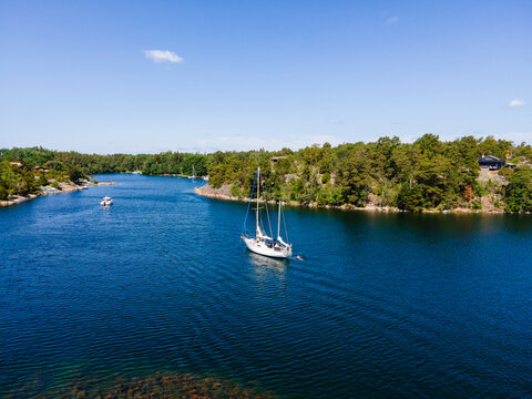 Aerial view of Vasterskaten in the Stockholm archipelago with a sailboat anchored in the blue water surrounded by pine forests and rocky shores Haro, Stockholm County, Sweden.