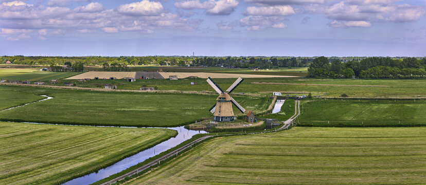 Bergen, Netherlands - 09 May 2026: Aerial view of the Philisteinsche Polder windmill in the Dutch countryside, surrounded by green fields, a canal, and flaglines on National Mill weekend.