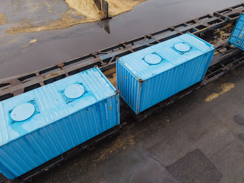Aerial view of bright blue shipping containers loaded on a train flatcar in a rail yard in Riga, Latvia.