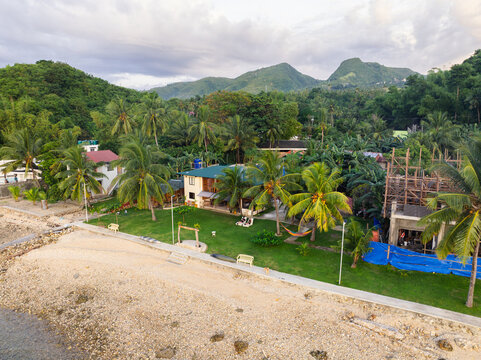Aerial view of a couple relaxing on chairs in a lush garden with palm trees and a house by the coast in Alegria, Central Visayas, Philippines.