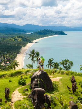 Aerial view of a couple standing on a rock at Ningning Viewpoint overlooking the sandy coastline of Erawan Beach, Boong Beach, and Nagtulay Beach in San Vicente, Mimaropa, Philippines.