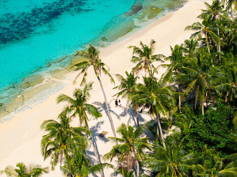 Aerial view of Puka Shell Beach in Boracay with lush palm trees, turquoise water, and a couple standing on the white sand in Malay, Western Visayas, Philippines.