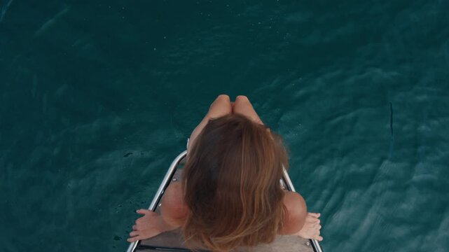 Young woman in sunglasses sits on the stern of the sailing boat and looks into the camera