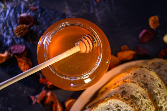 Golden honey and fresh bread slices beside glass jar in warm rustic kitchen setting