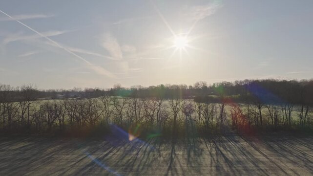 Late winter to early spring landscape drone aerial moving through rural Ohio farm field in country area outside city with fields of no plants, leaves, and dead trees with green yellow grass 4k