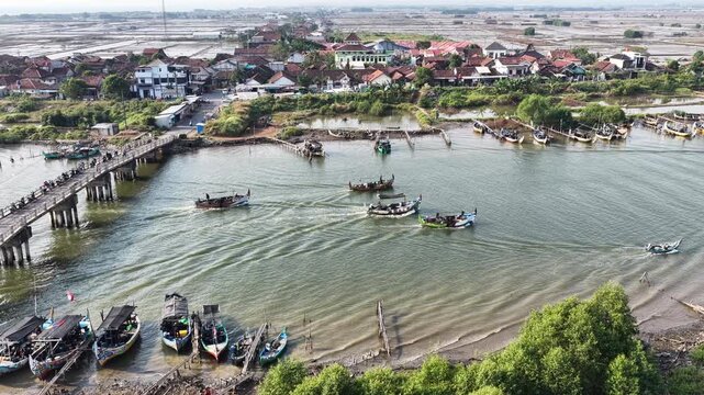 Aerial view of fishing boats in a bay near a wooden bridge and coastal village in Jepara, Central Java, Indonesia.