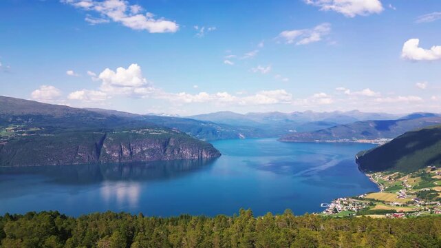 Aerial view of the village of Utvik nestled along the deep blue waters of the fjord with lush green forests and mountains in the background in Utvik, Vestland, Norway.