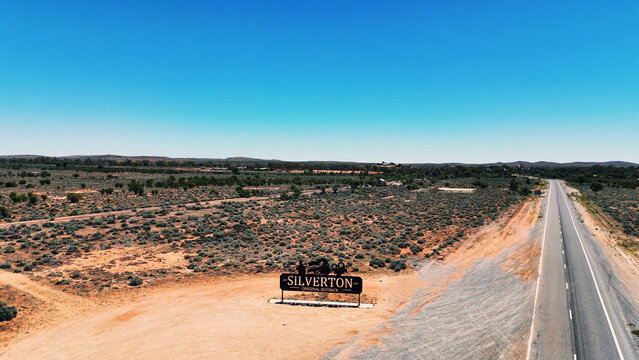 Silverton, New South Wales, Australia - 12 December 2024: Aerial view of the Silverton Sign in the arid outback landscape with a road stretching into the distance under a clear blue sky.