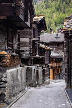View of traditional wooden houses with stone foundations lining a narrow cobblestone street in Zermatt, Valais, Switzerland.