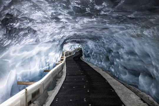 View of the ice tunnel at Matterhorn Glacier Paradise with translucent blue ice walls and a black walkway in Zermatt, Wallis, Switzerland.