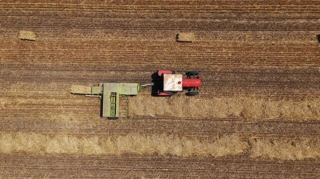 Aerial view of a red tractor pulling a green baler to collect hay in a harvested field in Jazak, Vojvodina, Serbia.